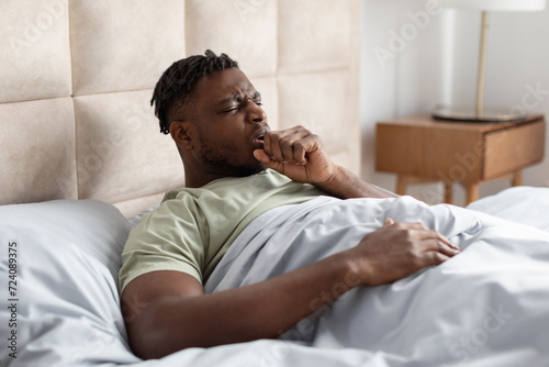 Sick Black Young Man Coughing In Fist Lying In Bed photo