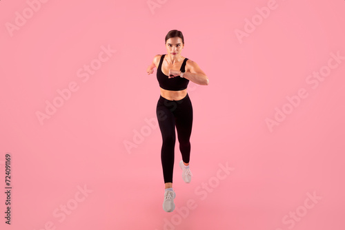 Determined female athlete running towards camera, training on pink background