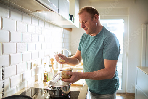 Middle aged man cooking and seasoning food in his kitchen photo