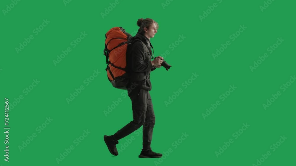 Side view of a male traveler taking photos on a camera during a hike. Man hiker in full length walking in studio on green screen. Concept of travel, active rest, hiking.