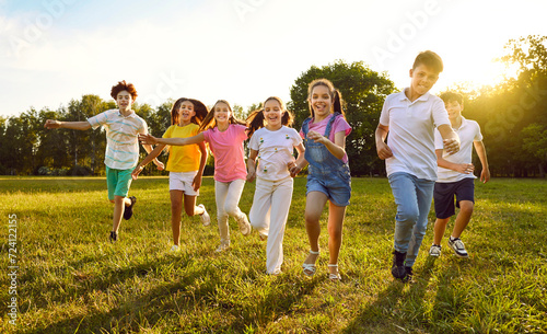 Happy, joyful, carefree kids playing together in summer. Children enjoying free time, playing and having fun. Group of cheerful little friends running on a grassy lawn in a green sunny park