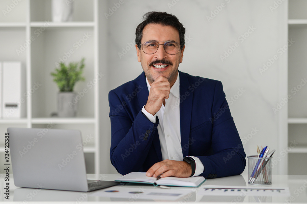 Smiling confident caucasian adult businessman in suit at table with computer laptop Smiling confident caucasian adult businessman in suit at table with computer laptop