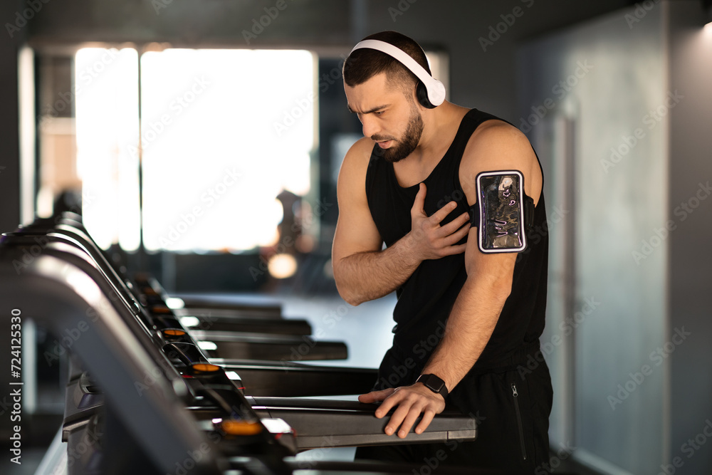 Distressed man experiencing sudden heartache while working out on treadmill at gym Distressed man experiencing sudden heartache while working out on treadmill at gym