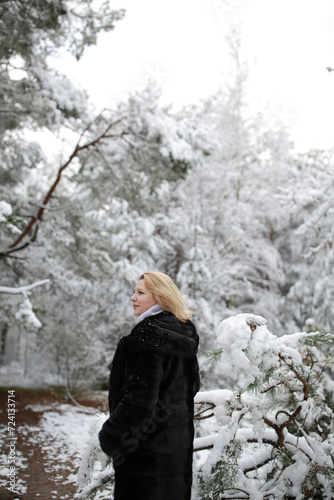 beautiful forty-year-old woman in a snowy forest. a woman in a fur black fur coat in winter in the forest. middle-aged woman near snowy trees