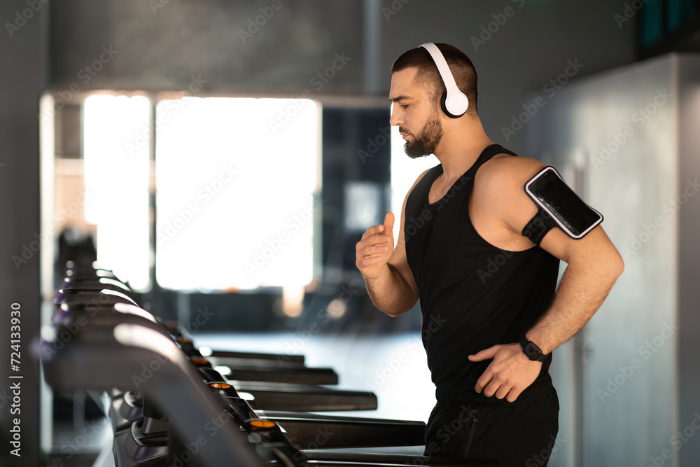 Handsome Masculine Man Wearing Wireless Headphones Running On Treadmill At Gym Handsome Masculine Man Wearing Wireless Headphones Running On Treadmill At Gym