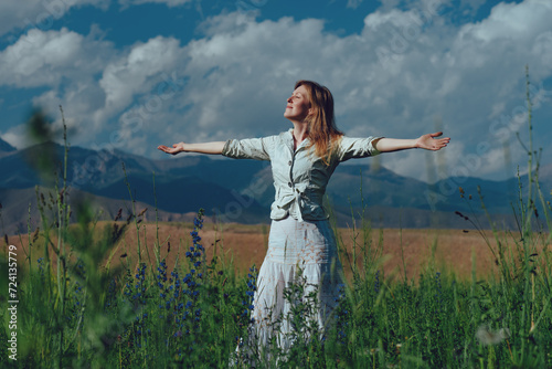 Happy young woman on summer field stretching arms and enjoying the day