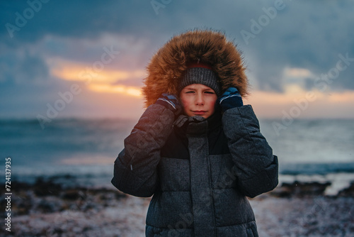 Portrait of boy in winter jacket with hood on seashore in stormy weather