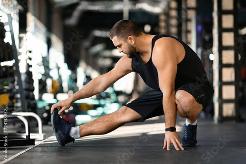 Fototapeta Naklejka Na Ścianę i Meble -  Handsome young man performing leg stretch before workout in gym