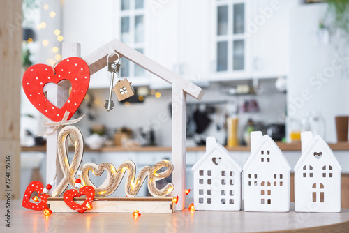 Key to tiny house of cozy home with Valentine decor on table of kitchen. Gift for valentines day, family love nest. design, project, moving to new house, mortgage, rent and purchase real estate