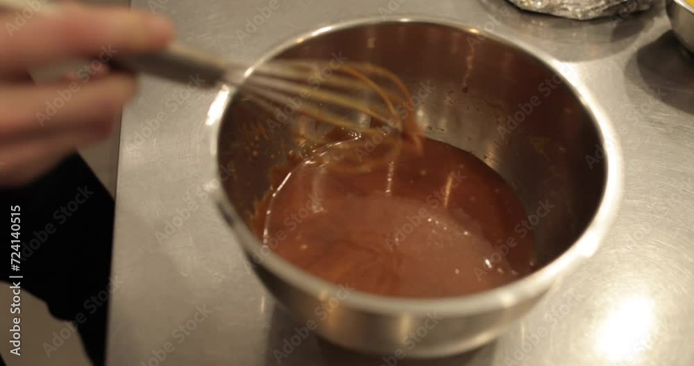 Mixing the chocolate glaze in a round metal bowl with a whisk. Close-up of hands stirring chocolate mousse with a whisk. Professional confectionery. Mixing the chocolate glaze in a round metal bowl with a whisk. Close-up of hands stirring chocolate mousse with a whisk. Professional confectionery.