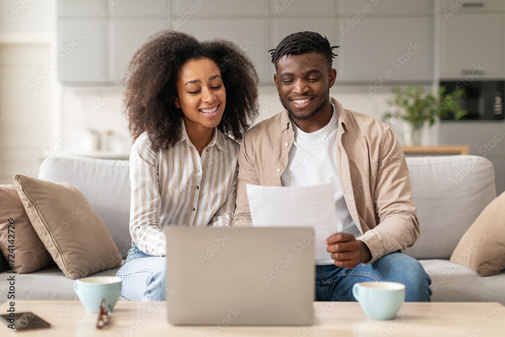 Happy black spouses paying bills via laptop holding papers indoor Happy black spouses paying bills via laptop holding papers indoor
