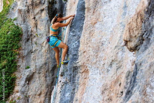 A young and strong woman is rock climbing on a rock.