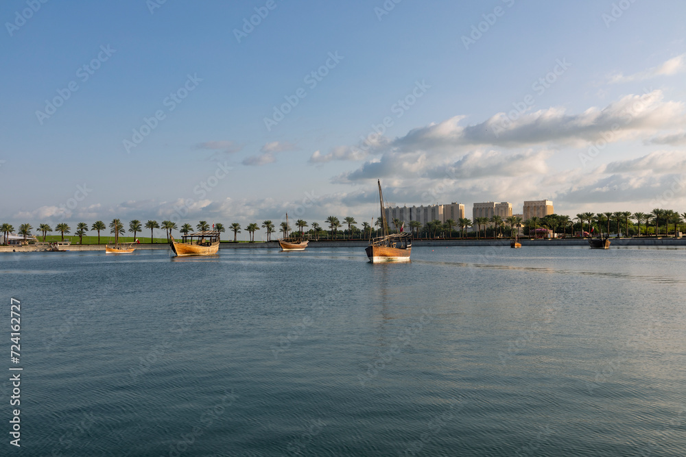 A view of the garden of the Museum of Islamic Art in Qatar, with the sea, boats and palm trees, with Doha Towers 