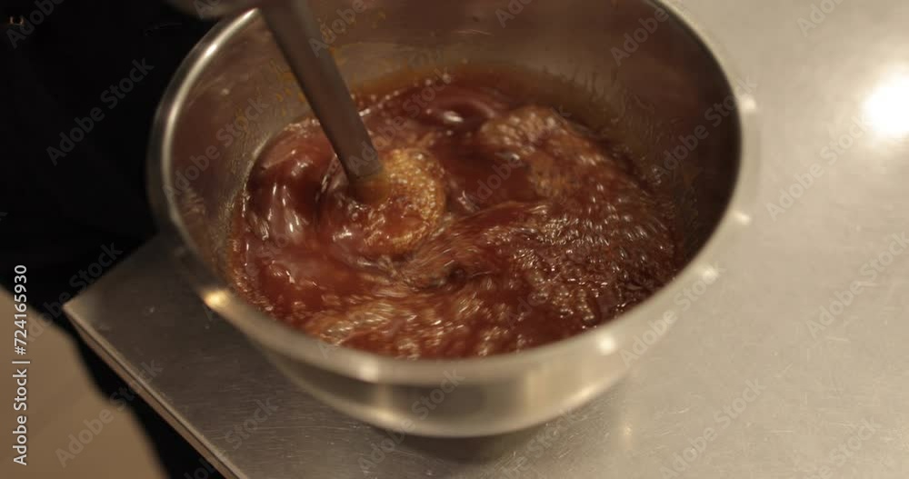 Mixing the chocolate glaze in a round metal bowl with a whisk. Close-up of hands stirring chocolate mousse with a whisk. Professional confectionery. Mixing the chocolate glaze in a round metal bowl with a whisk. Close-up of hands stirring chocolate mousse with a whisk. Professional confectionery.
