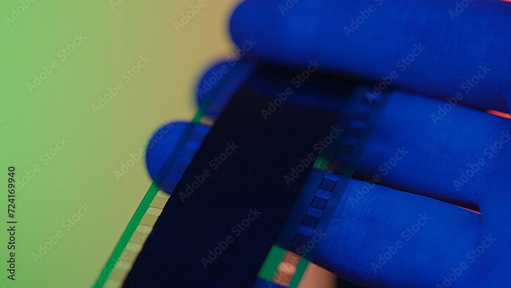 Reviewing a negative photo film strip. Photographic film in men's hands in red, blue and green neon light close up.