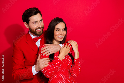 Photo portrait of stunning young couple hug look empty space valentine day dressed stylish elegant garment isolated on red color background