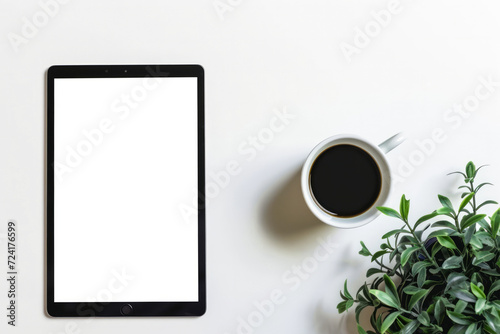 Empty electronic tablet on a table next to a cup of coffee and a plant. Use as a template or mockup