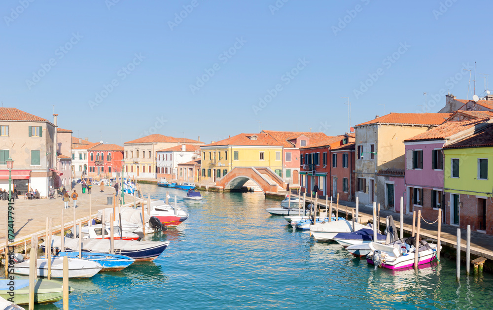 Murano islands, bridge across water canal, boats and motor boats, colorful traditional buildings, Venetian Lagoon, Veneto Region, Northern Italy. San Michele in Isola Catholic church background