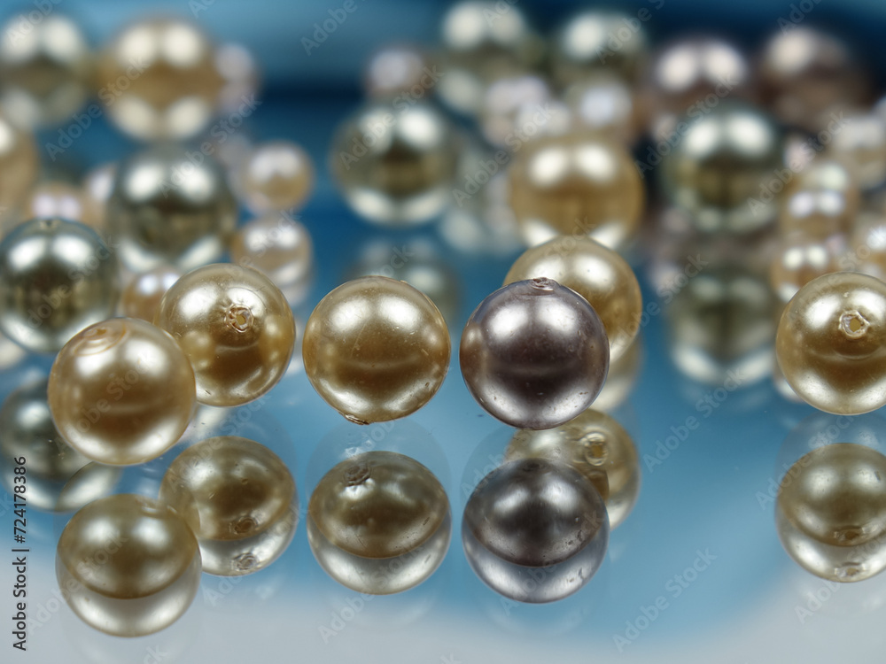 Pearl beads of various colors lie on the mirror and are reflected in it against the background of blue satin fabric. Pearl beads of various colors lie on the mirror and are reflected in it against the background of blue satin fabric.