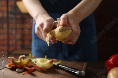 Woman peeling fresh potato at table indoors, closeup photo