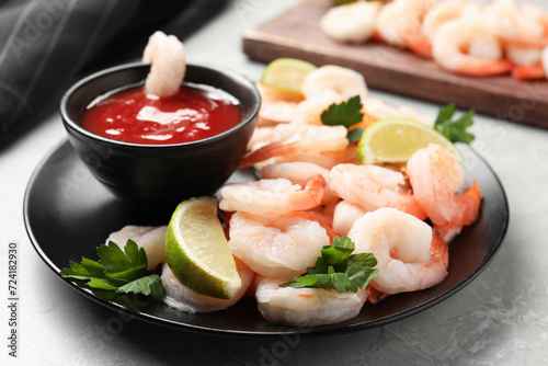 Tasty boiled shrimps with cocktail sauce, parsley and lime on light grey table