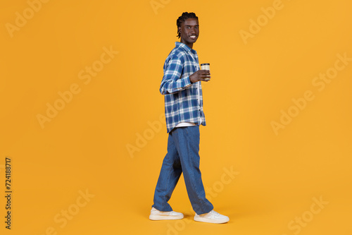 Relaxed young black man walking with takeaway coffee cup in hand