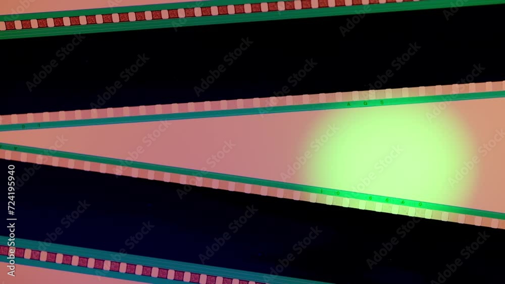 Two black film strips on pink background illuminated with green neon circular light, close up. Copy space. Two black film strips on pink background illuminated with green neon circular light, close up. Copy space.