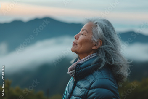 A senior woman doing breathing exercise in nature on early morning with background of mountains