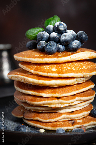 Pile of pancakes with blueberries on a plate on a dark background 