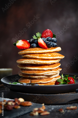 Pile of pancakes with blueberries and strawberries on a plate with dark background  