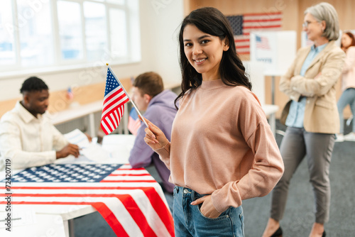 Portrait of smiling woman, voter holding American flag waiting in line at polling station. Democracy, freedom, vote, United States presidential election concept photo