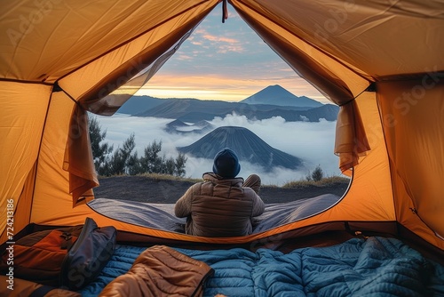 As the sun rises over the majestic mountains, a lone figure sits in their tent, surrounded by their camping equipment and protected by a tarpaulin, lost in the peacefulness of the great outdoors