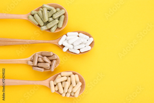 Different vitamin capsules in wooden spoons on yellow background, flat lay. Space for text photo