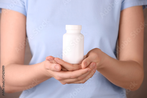 Woman holding blank white bottle with vitamin pills, closeup