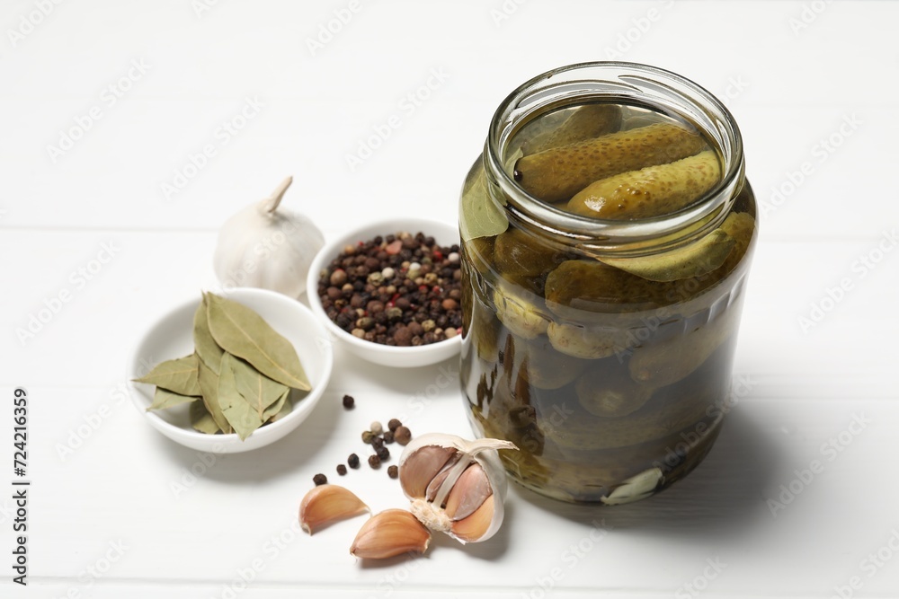 Tasty pickled cucumbers in jar and ingredients on white wooden table Tasty pickled cucumbers in jar and ingredients on white wooden table