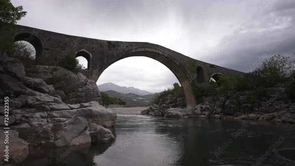 Historic old stone bridge in Shkodër Albania, wide angle view of a river with mountains and clouds in the sky