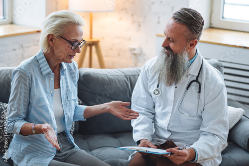 Senior male doctor examining his patient mature attractive woman during home or clinic visit. Healthcare for elderly retired people, insurance. Illness, disease diagnosis, treatment prescription photo