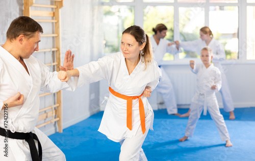 Woman is paired with man teacher to learn how to strike and rehearses blocking opponent, using karate technique