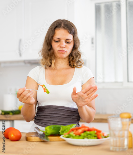 Portrait of discontented woman eating salad at home. Sad woman dinning with fresh vegetable salad.