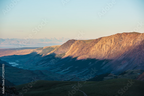 Scenic aerial top view to gold sheer crags on mountain ridge, illuminated by setting sun under clear sky in golden sunset tones. Evening alpine landscape in sunset color. Light and shadow in mountains
