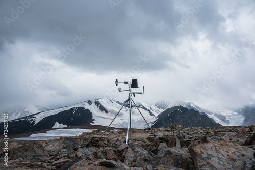 Automatic meteorological station on stone hill with view to large snow-capped mountain range. Measurement speed and direction of wind among glaciers. Measuring atmospheric pressure and precipitation.