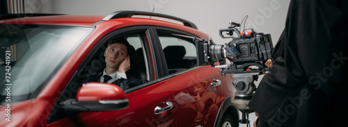 Professional male actor works in the frame on the set. Shooting with a car on a large white cyclorama.