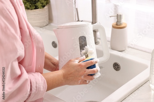 Woman washing electric kettle with sponge at sink in kitchen, closeup photo
