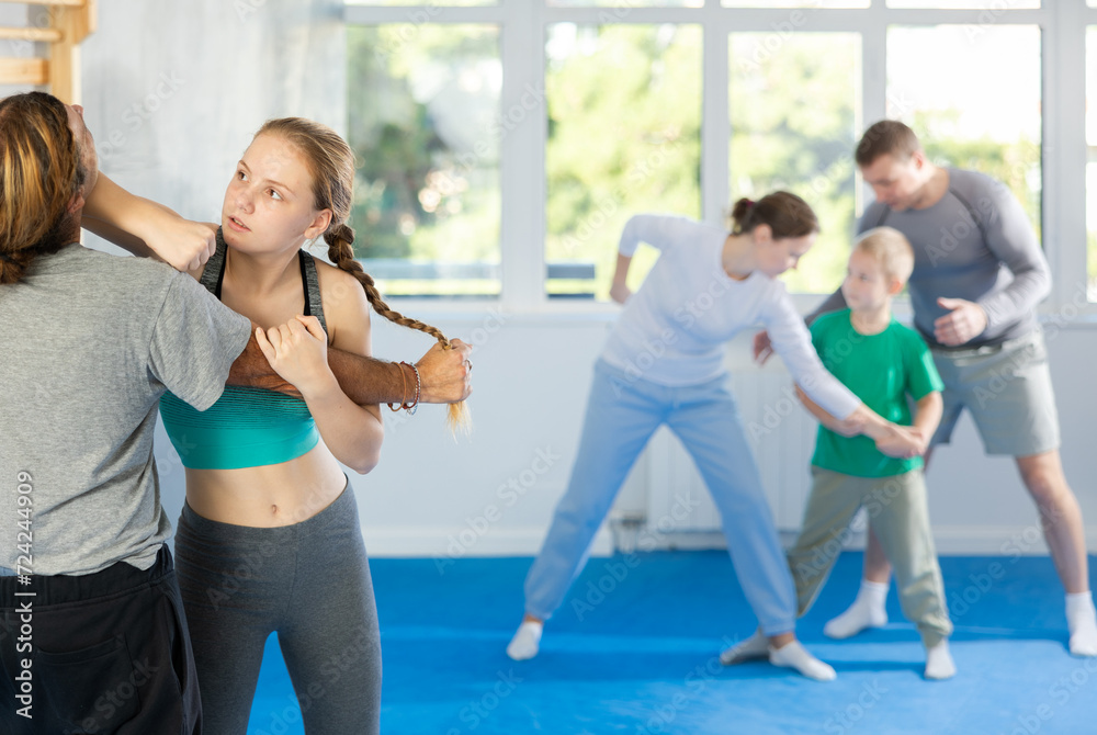 Man and teen girl at group self-defense lesson are learning new technique of blowing to chin, trainer is practicing technique with other pair in background
