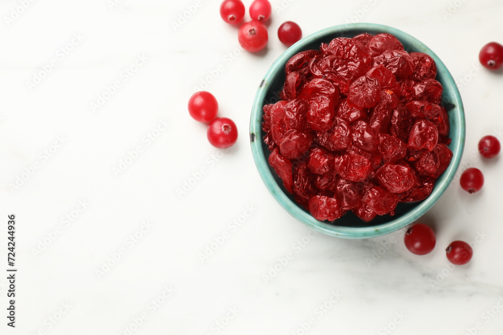 Tasty dried cranberries in bowl and fresh ones on white table, top view. Space for text Tasty dried cranberries in bowl and fresh ones on white table, top view. Space for text