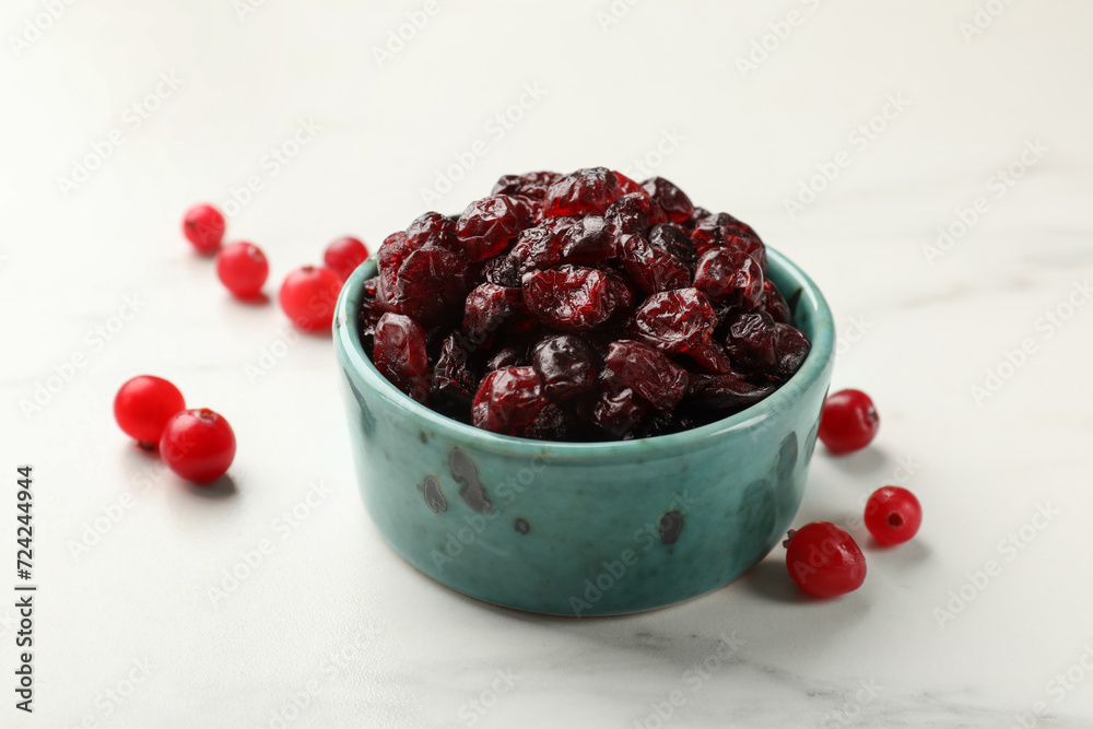 Tasty dried cranberries in bowl and fresh ones on white marble table, closeup Tasty dried cranberries in bowl and fresh ones on white marble table, closeup