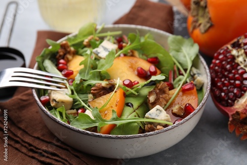 Tasty salad with persimmon, blue cheese, pomegranate and walnuts served on light grey table, closeup