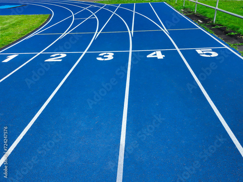Blue running track with starting line numbers one to five. Isolated on blue background for sports and athletics concept. Empty track for copy space and text overlay. Top view of running track.