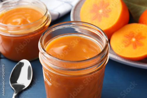 Delicious persimmon jam in glass jars served on blue table, closeup