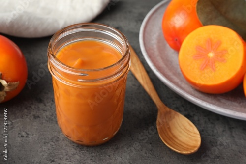 Delicious persimmon jam in glass jar served on gray table, closeup